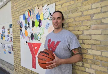 Joshua Gandier stands in front of brick wall and art at the Downtown Y