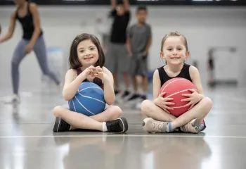 Two young girls sitting with basketballs smiling at camera