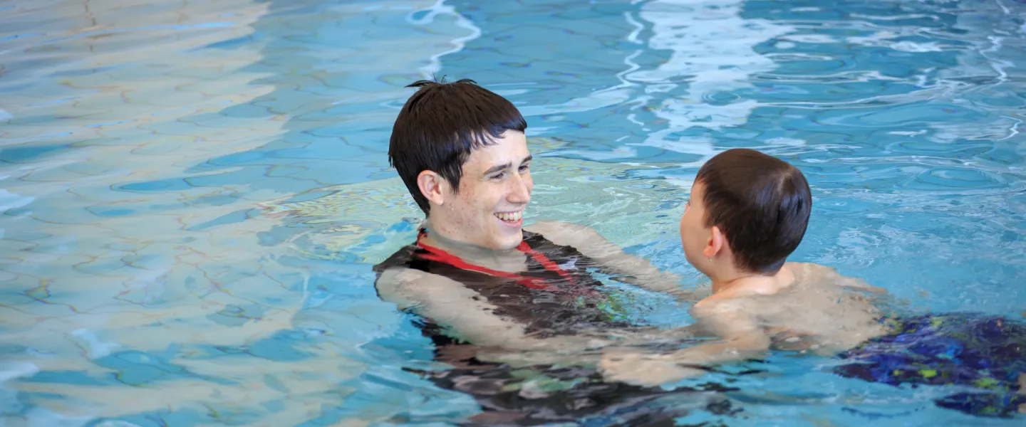 smiling male swim instructor teaching young swimmer in pool