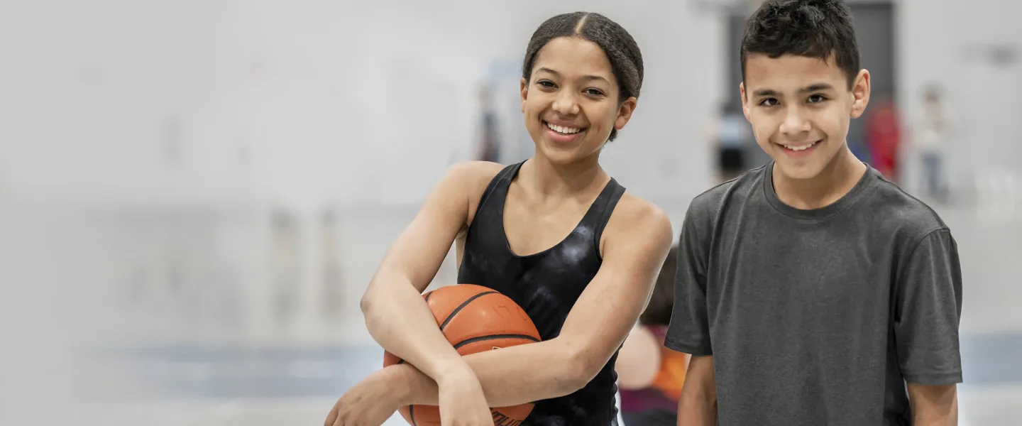 Image of boy and girl posing on basketball court. girl holding basketball.