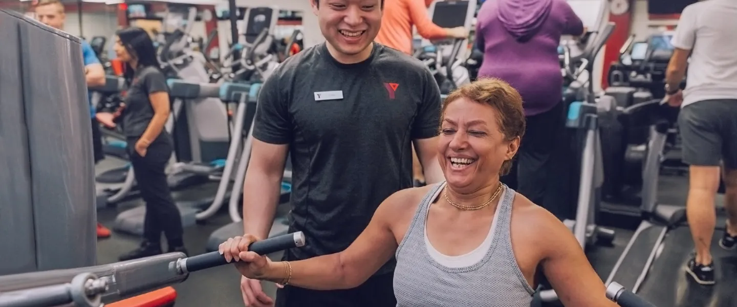 Fitness Staff With Woman Using Resistance Equipment