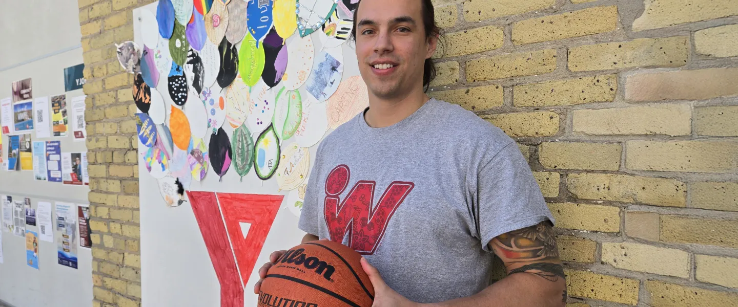 Joshua Gandier stands in front of brick wall and art at the Downtown Y