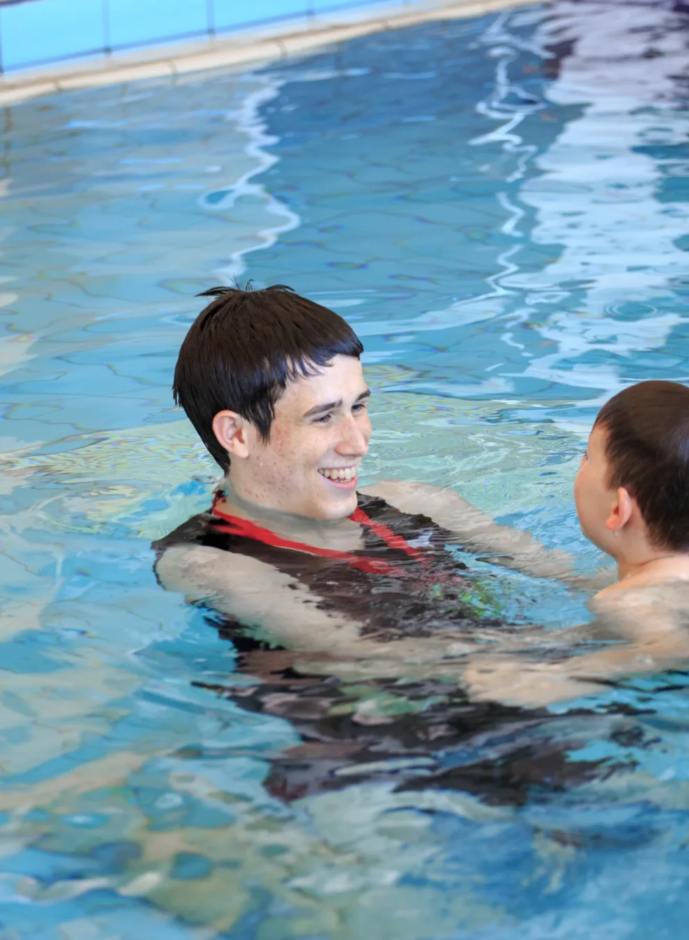 smiling male swim instructor teaching young swimmer in pool