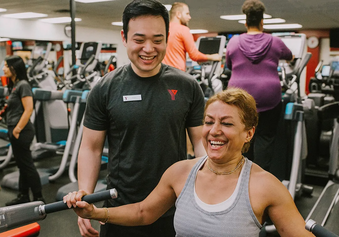 Fitness Staff With Woman Using Resistance Equipment