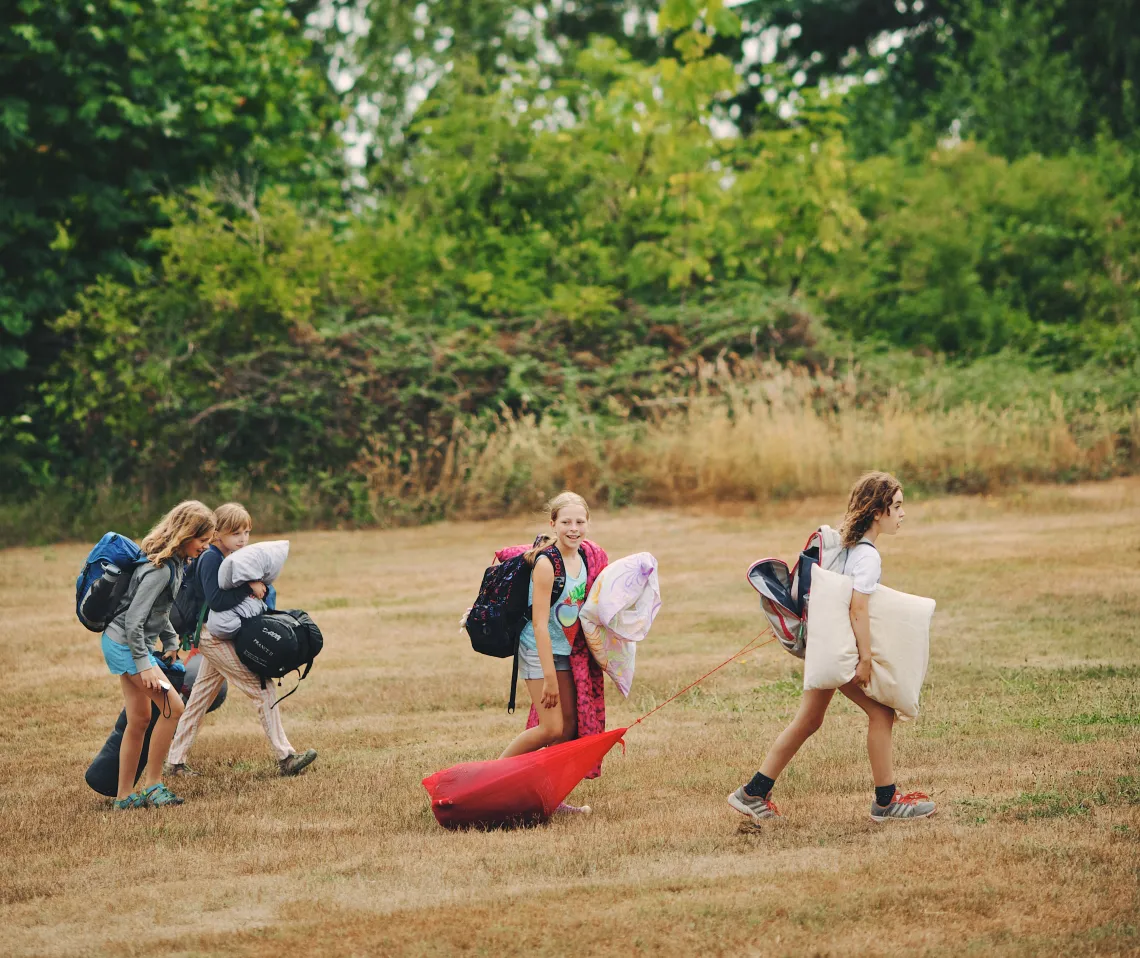 Young female campers with overnight bags walking across the lawn