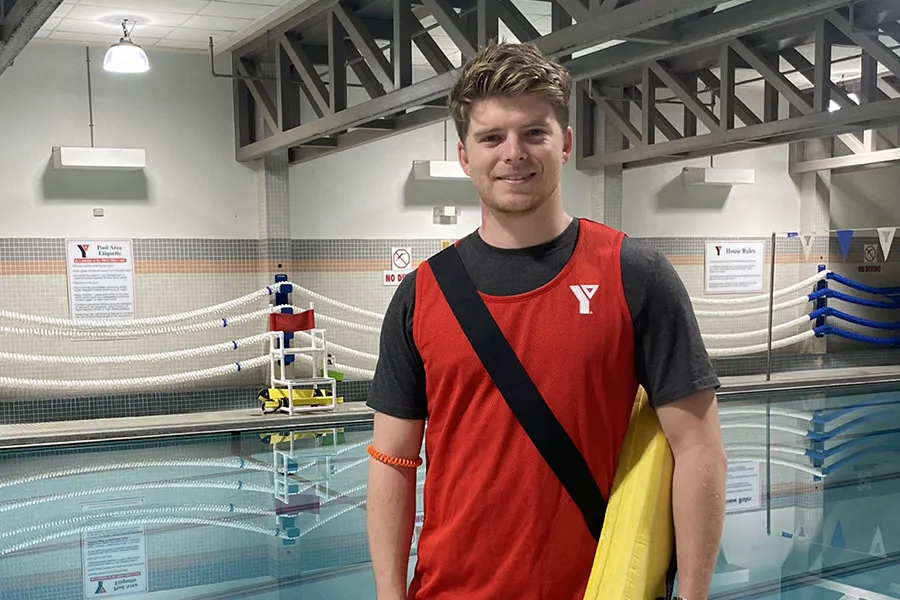 Lifeguard at Downtown Y standing in front of the pool holding flotation device