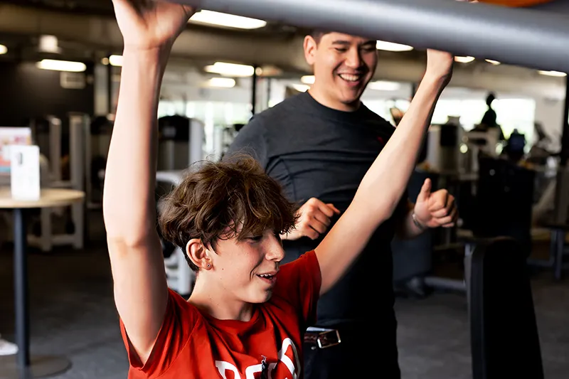 YMCA staff assisting youth trying strength equipment