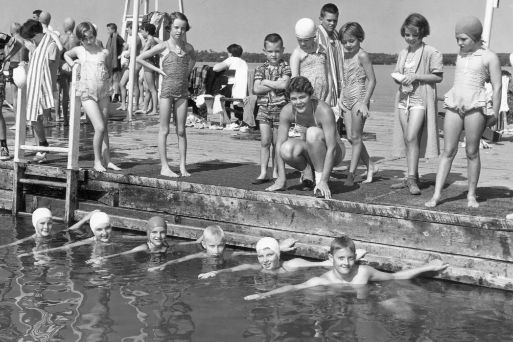 black and white image of swimming lessons. kids in water at a dock, instructor looking on