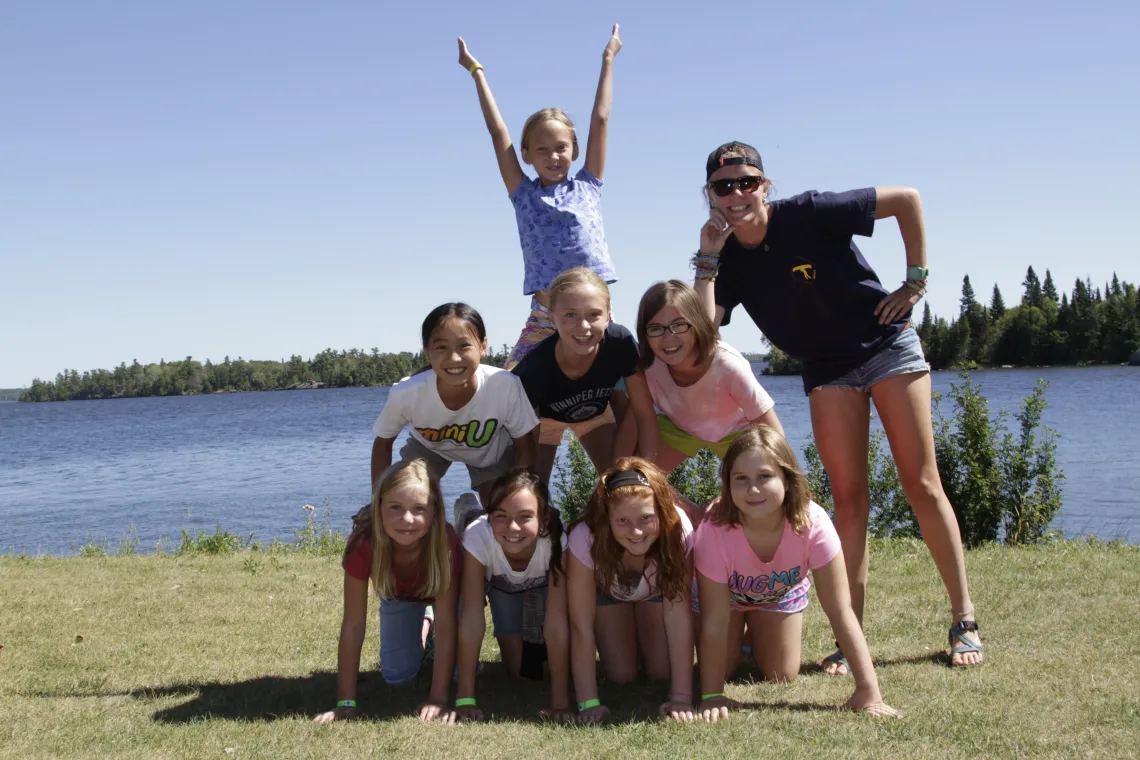 Image of 8 smiling girls creating a human pyramid on the shore with a female camp counsellor 