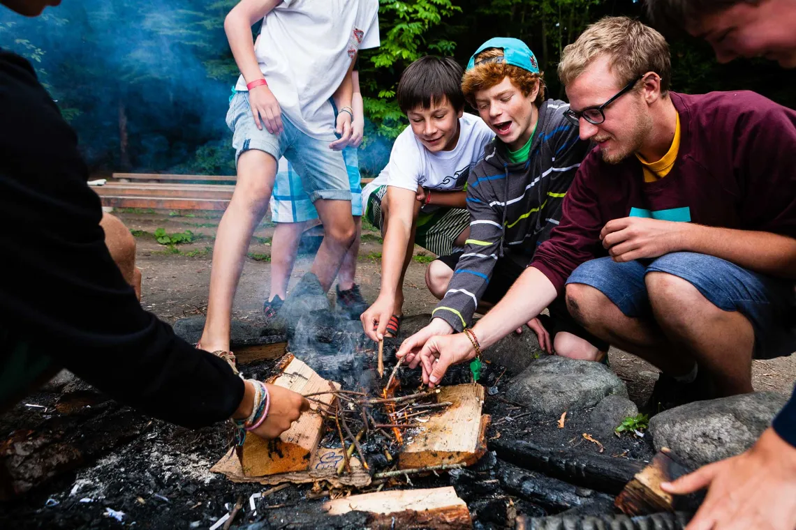 Male teenage campers with their Counsellor starting a bonfire.