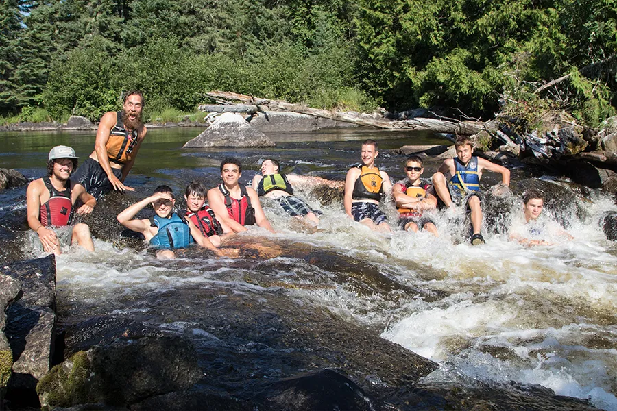 group of campers in life-jackets sitting in a small rapid