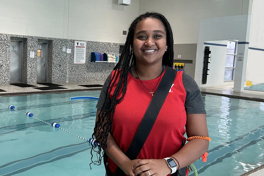 Smiling black female lifeguard standing in front of pool