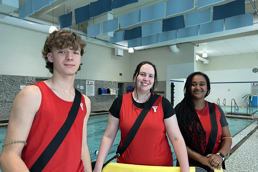 three smiling Y Winnipeg lifeguards next to a pool