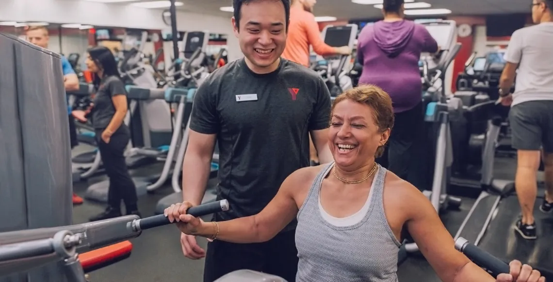 Fitness Staff With Woman Using Resistance Equipment