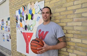 Joshua Gandier stands in front of brick wall and art at the Downtown Y