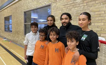 Image of the Fekiri family at the Downtown Y. Triplet boys stand in front wearing orange with older sister, father, mother and older brother in the back row. 