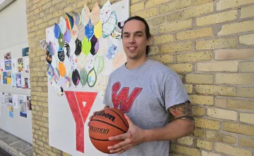 Joshua Gandier stands in front of brick wall and art at the Downtown Y